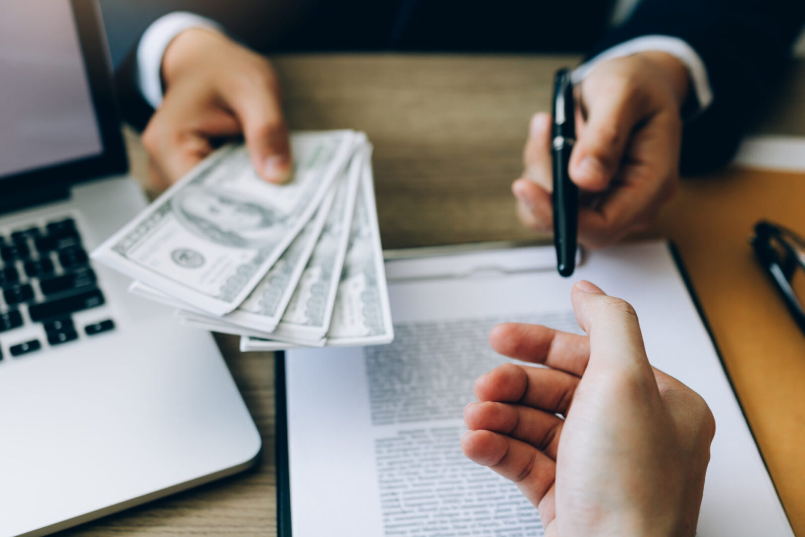 Hands exchanging money and signing a document.