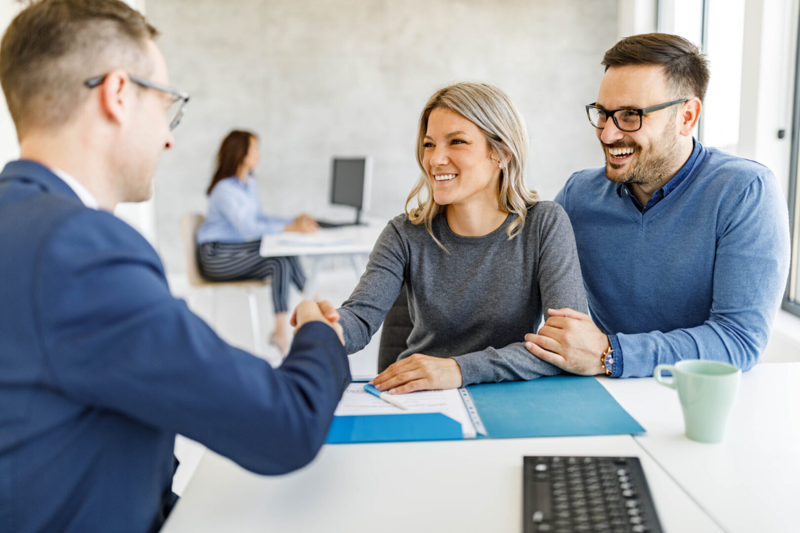 Young happy couple reached a successful deal with their insurance agent on a meeting in the office. Focus is on woman.